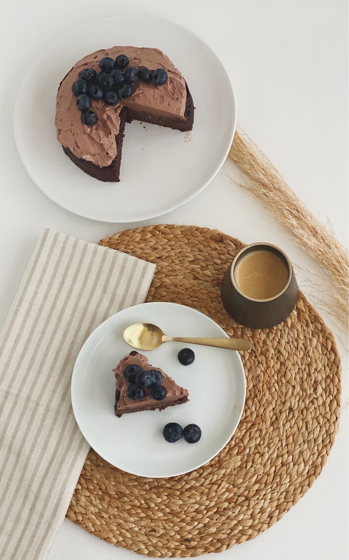 Chokoladekage med avocado med kakaosmørcreme og pyntet med blåbær på toppen, set oppefra og den hele kage ses + et enkelt stykke for sig selv og en kop kaffe som står på en siv dækkeserviet